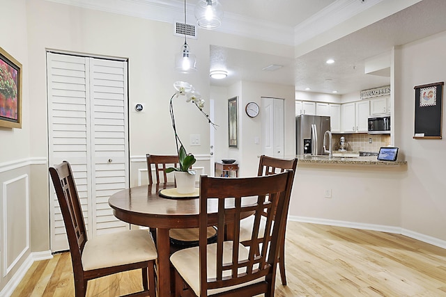 dining room featuring sink, crown molding, and light hardwood / wood-style flooring