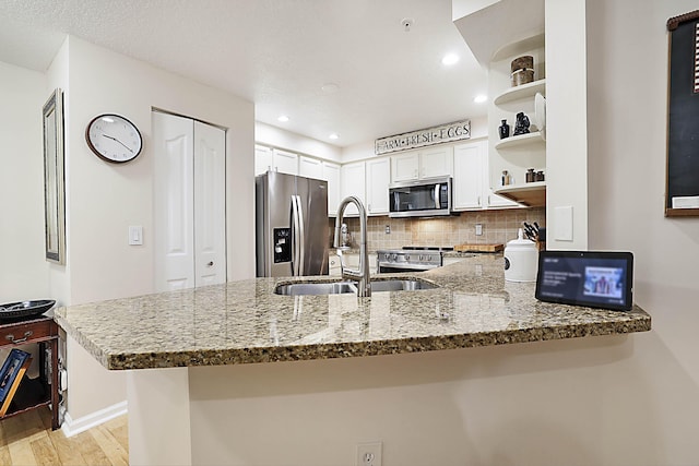 kitchen featuring appliances with stainless steel finishes, sink, white cabinets, light stone counters, and kitchen peninsula