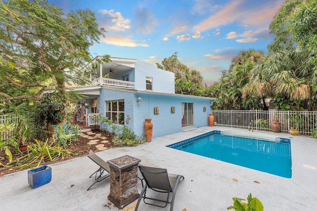 pool at dusk with ceiling fan, a patio area, and a fire pit