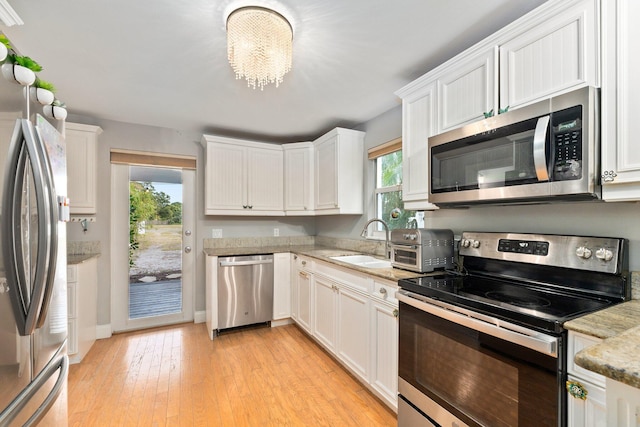 kitchen with white cabinetry, appliances with stainless steel finishes, a notable chandelier, light wood-type flooring, and sink