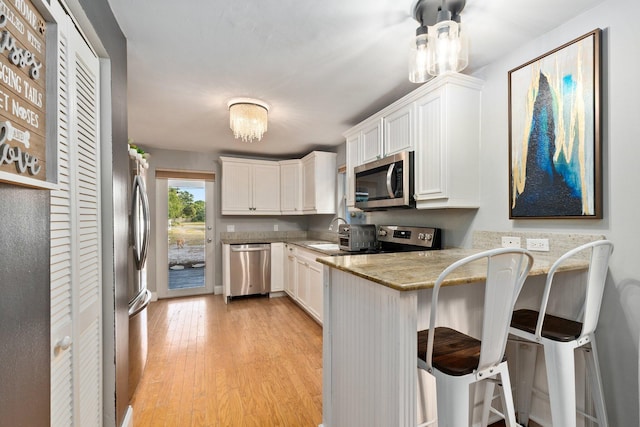 kitchen with light hardwood / wood-style floors, kitchen peninsula, appliances with stainless steel finishes, a kitchen breakfast bar, and white cabinets