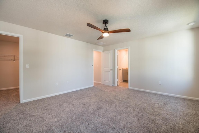 unfurnished bedroom with a walk in closet, connected bathroom, a closet, ceiling fan, and light colored carpet