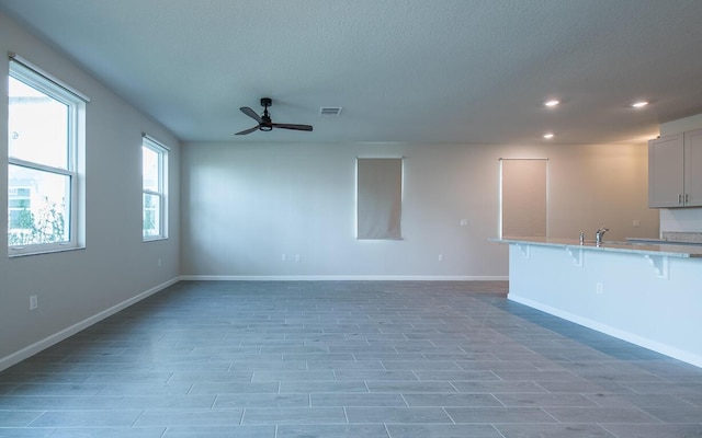 unfurnished living room featuring ceiling fan, sink, and a textured ceiling