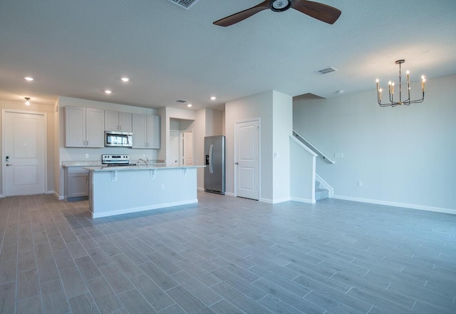 kitchen featuring a center island with sink, stainless steel appliances, decorative light fixtures, ceiling fan with notable chandelier, and a breakfast bar