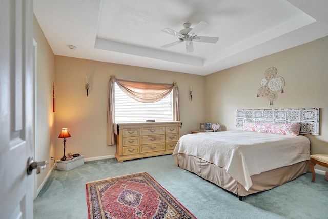 carpeted bedroom featuring a tray ceiling and ceiling fan