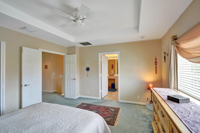 bedroom with light carpet, a raised ceiling, ceiling fan, and ensuite bathroom