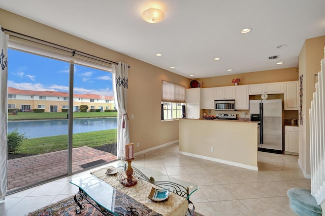 kitchen with a water view, light tile patterned floors, appliances with stainless steel finishes, a kitchen island, and white cabinets