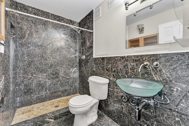 bathroom featuring tiled shower, toilet, tile walls, and sink