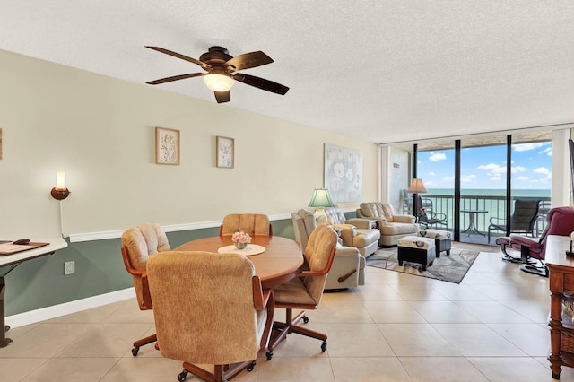 dining area featuring a textured ceiling, ceiling fan, a wall of windows, and a water view