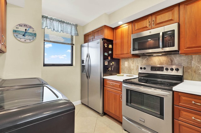 kitchen featuring washer and clothes dryer, backsplash, light tile patterned floors, and stainless steel appliances