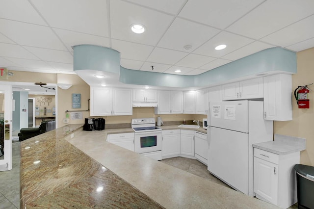 kitchen featuring white appliances, white cabinets, kitchen peninsula, and a drop ceiling