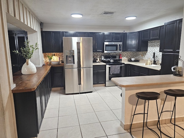 kitchen with light tile patterned floors, a kitchen bar, appliances with stainless steel finishes, decorative backsplash, and sink