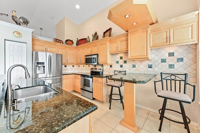 kitchen with stainless steel appliances, a kitchen breakfast bar, decorative backsplash, dark stone counters, and light brown cabinets