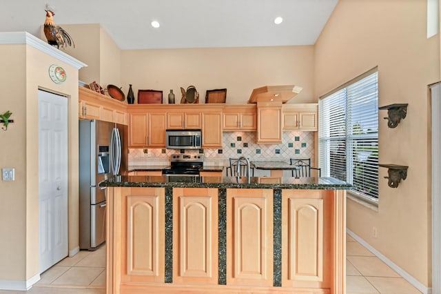 kitchen with stainless steel appliances, an island with sink, light tile patterned flooring, and light brown cabinetry