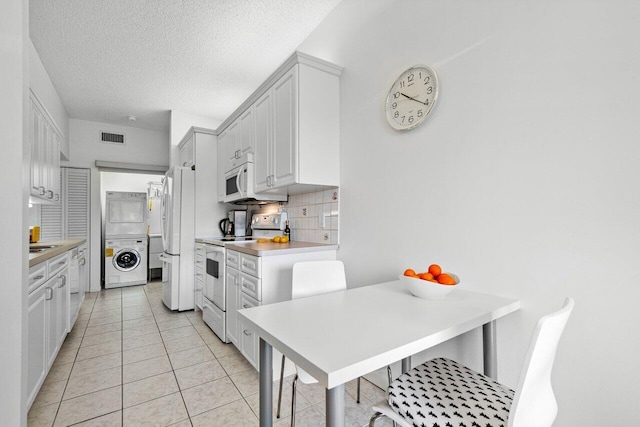 kitchen featuring a breakfast bar, tasteful backsplash, stacked washer / dryer, white cabinets, and white appliances