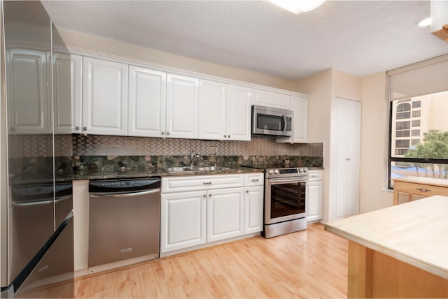 kitchen with sink, appliances with stainless steel finishes, tasteful backsplash, a textured ceiling, and white cabinets