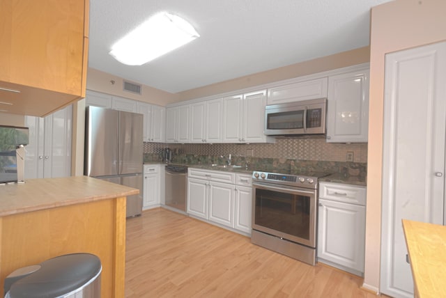 kitchen featuring white cabinetry, stainless steel appliances, light hardwood / wood-style floors, and backsplash