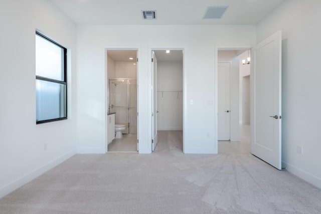 unfurnished bedroom featuring light carpet, a closet, ensuite bath, and a spacious closet