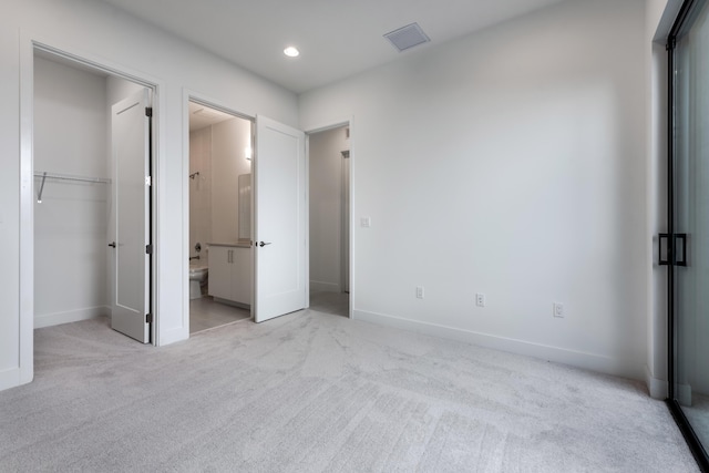 unfurnished bedroom with a closet, connected bathroom, and light colored carpet