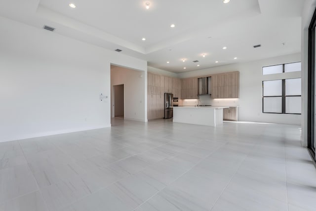 unfurnished living room featuring sink, light tile patterned floors, and a raised ceiling