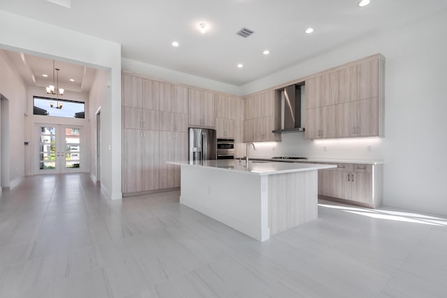 kitchen featuring pendant lighting, wall chimney range hood, sink, stainless steel fridge, and a center island with sink