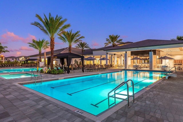 pool at dusk featuring a hot tub and a patio