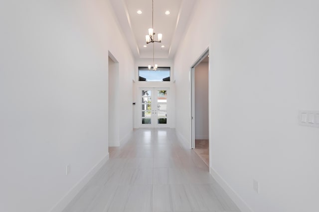 hall featuring french doors, light tile patterned floors, a tray ceiling, a high ceiling, and a notable chandelier