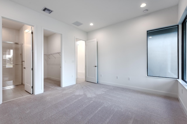 unfurnished bedroom with a closet, connected bathroom, light colored carpet, and a spacious closet