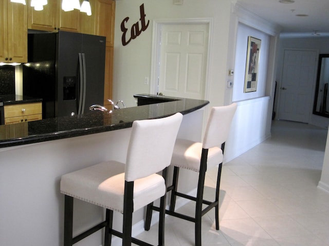 kitchen with a breakfast bar, dark stone countertops, light tile patterned floors, kitchen peninsula, and black refrigerator with ice dispenser