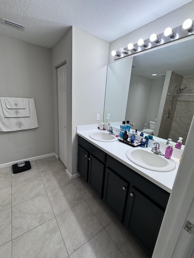 bathroom with vanity, tile patterned flooring, tiled shower, and a textured ceiling