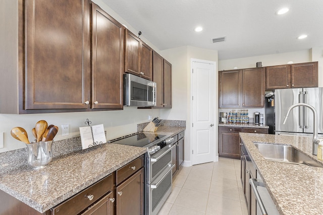 kitchen featuring sink, appliances with stainless steel finishes, light tile patterned floors, dark brown cabinets, and stone countertops