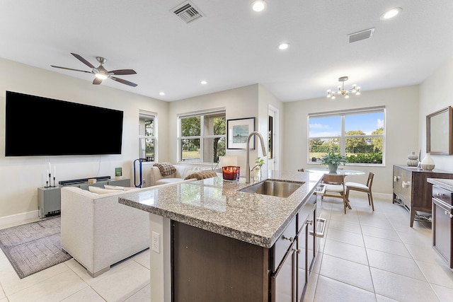 kitchen with a healthy amount of sunlight, an island with sink, light stone counters, and sink