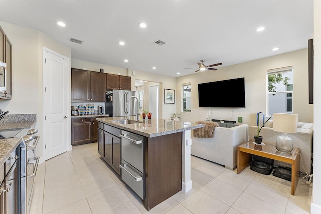 kitchen with ceiling fan, stainless steel appliances, a kitchen island with sink, light stone countertops, and sink