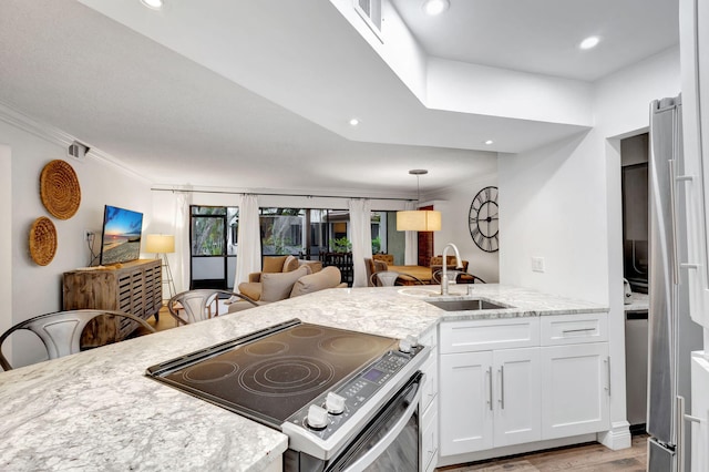 kitchen featuring appliances with stainless steel finishes, white cabinetry, sink, kitchen peninsula, and light wood-type flooring