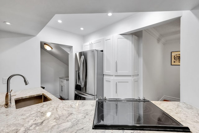 kitchen with white cabinetry, sink, stainless steel fridge, light stone counters, and black electric cooktop