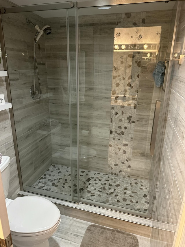 bathroom featuring a shower with door and toilet