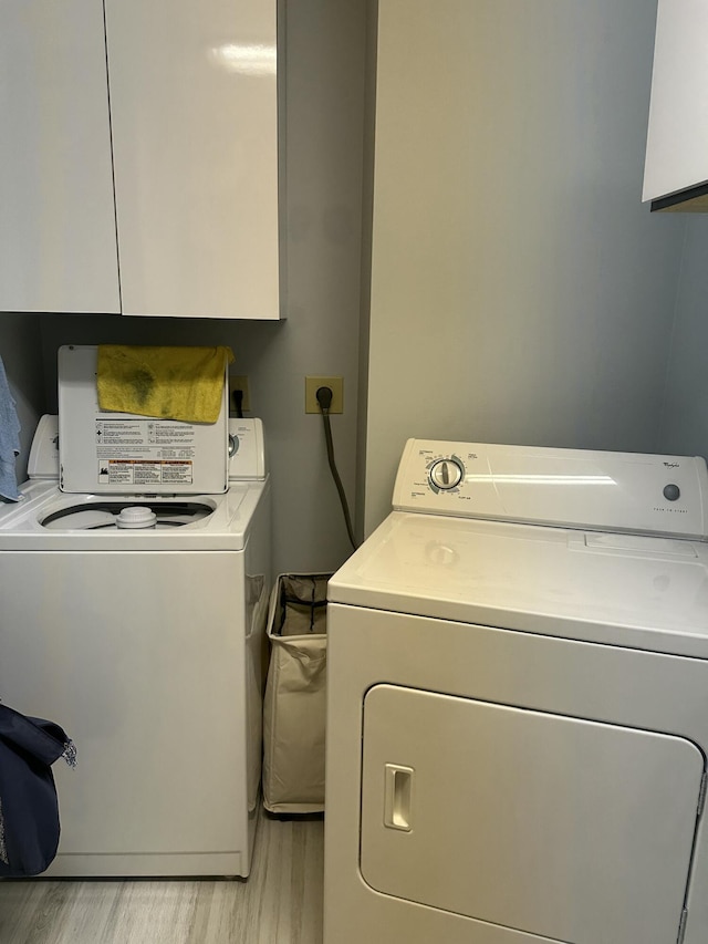 laundry area with separate washer and dryer, light hardwood / wood-style floors, and cabinets