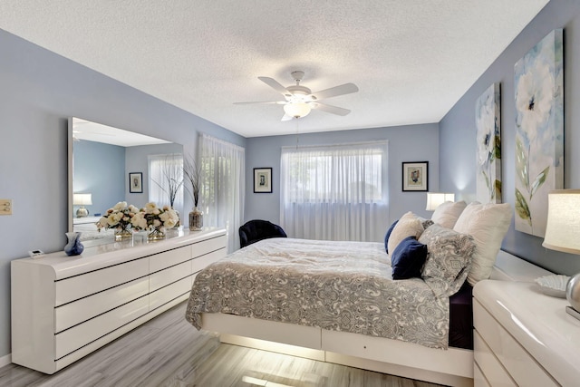 bedroom with ceiling fan, light hardwood / wood-style floors, and a textured ceiling