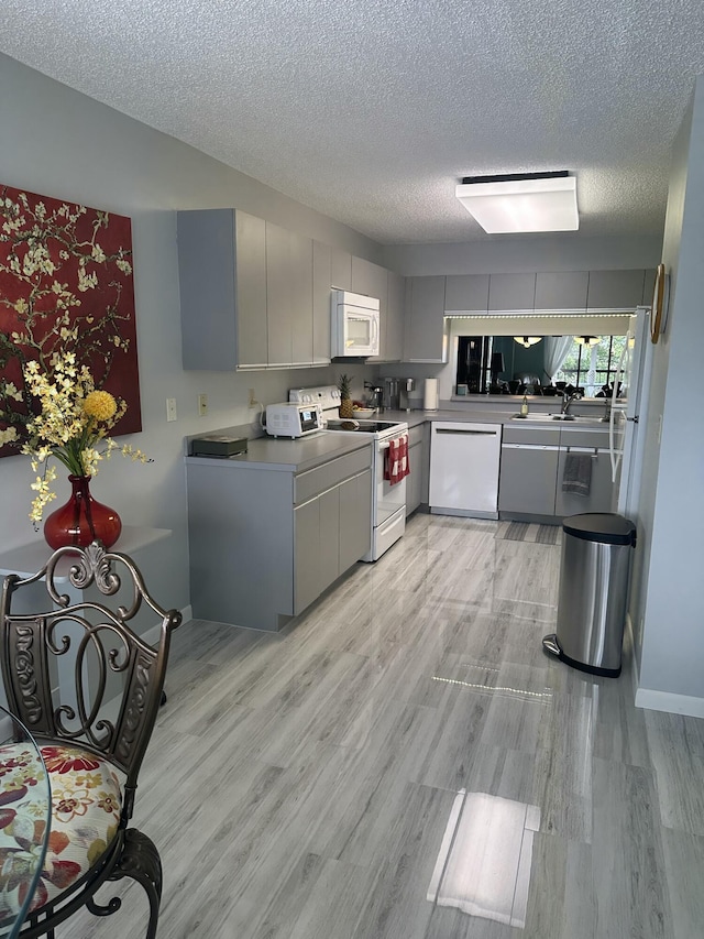 kitchen with white appliances, light hardwood / wood-style flooring, a textured ceiling, and gray cabinetry