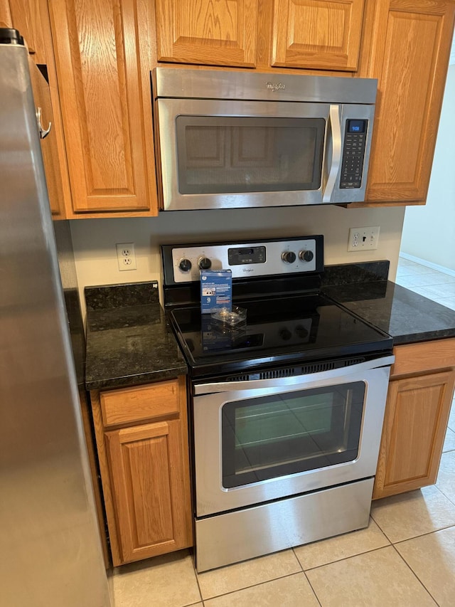 kitchen featuring light tile patterned floors, stainless steel appliances, and dark stone countertops