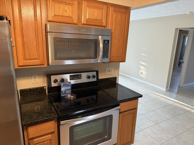 kitchen featuring light tile patterned floors, appliances with stainless steel finishes, and dark stone countertops