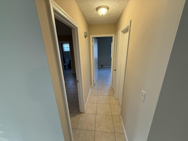 hallway with a textured ceiling and light tile patterned floors