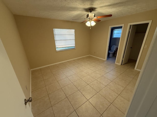 unfurnished bedroom with ensuite bathroom, ceiling fan, a spacious closet, a textured ceiling, and light tile patterned floors