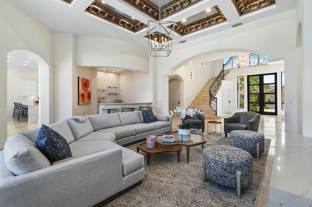 living room featuring coffered ceiling, a chandelier, a towering ceiling, and french doors