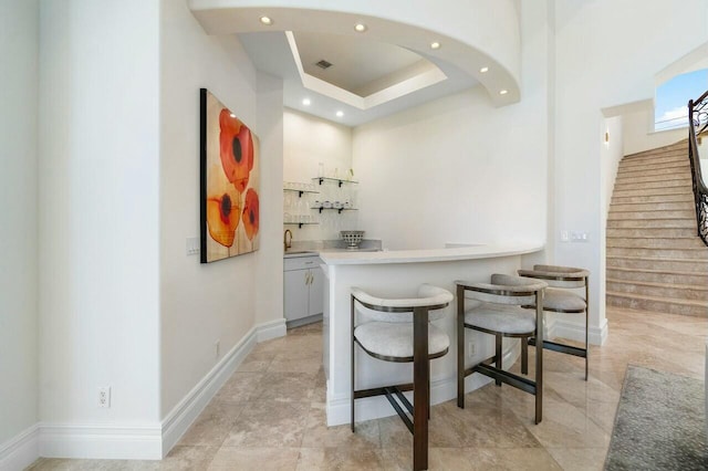 bar featuring a raised ceiling, white cabinets, and sink