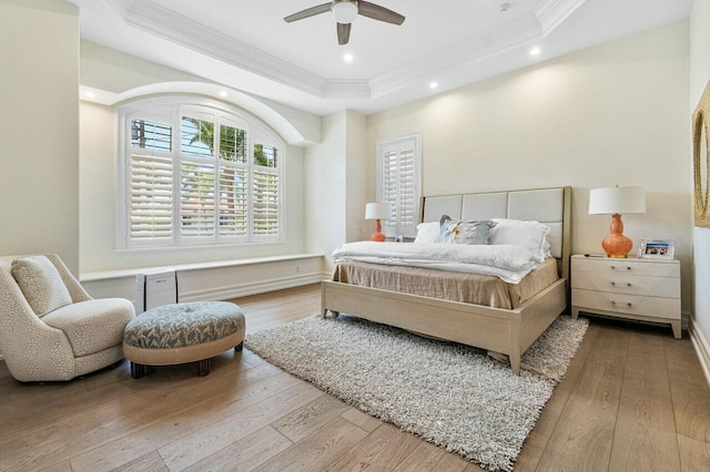 bedroom with ceiling fan, light hardwood / wood-style floors, crown molding, and a raised ceiling