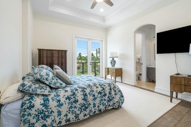 bedroom with ceiling fan, access to exterior, hardwood / wood-style floors, ensuite bath, and a tray ceiling