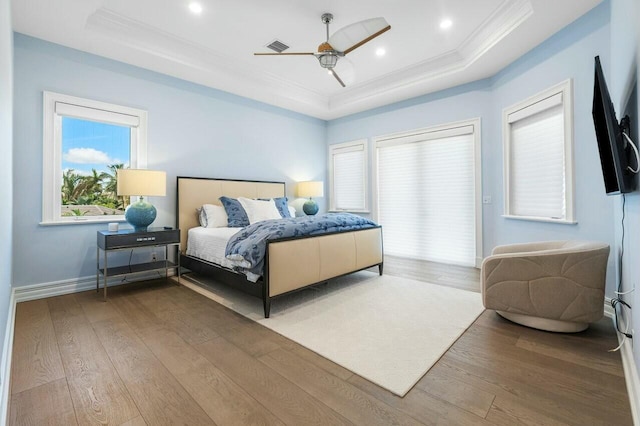 bedroom featuring ceiling fan, hardwood / wood-style floors, a tray ceiling, and multiple windows