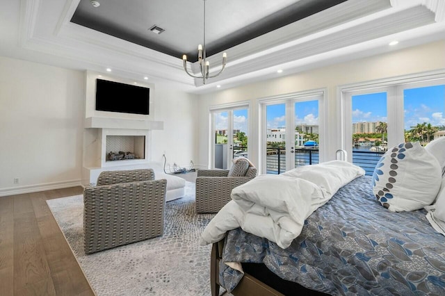 bedroom featuring french doors, access to exterior, a chandelier, hardwood / wood-style flooring, and a tray ceiling