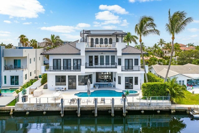 rear view of house with a balcony, a patio area, a swimming pool with hot tub, and a water view